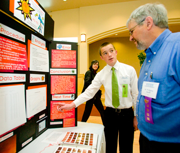 Young student showing science fair project to judge