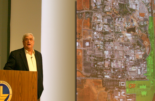 Director Miller speaking with an arial view of the campus